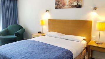A hotel room with a large bed, a green armchair, two bedside tables with lamps, and a wall-mounted picture.
