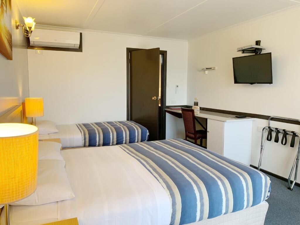 A hotel room with a bed, bedside lamp, desk, chair, TV, and a coat rack.