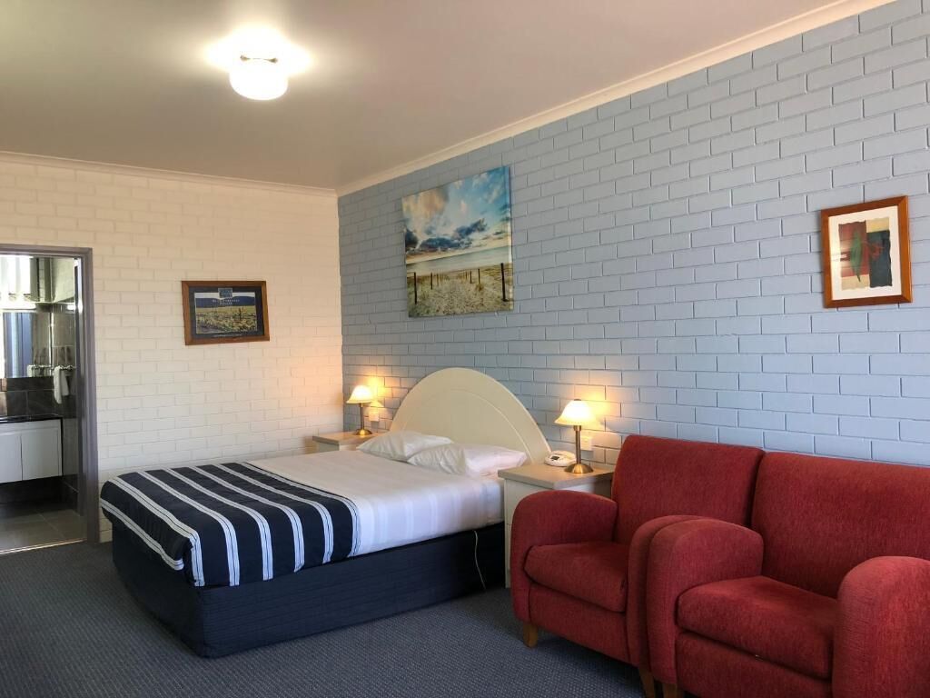 Una habitación de hotel con una cama, una silla roja, un muro de ladrillo blanco y un cuadro.