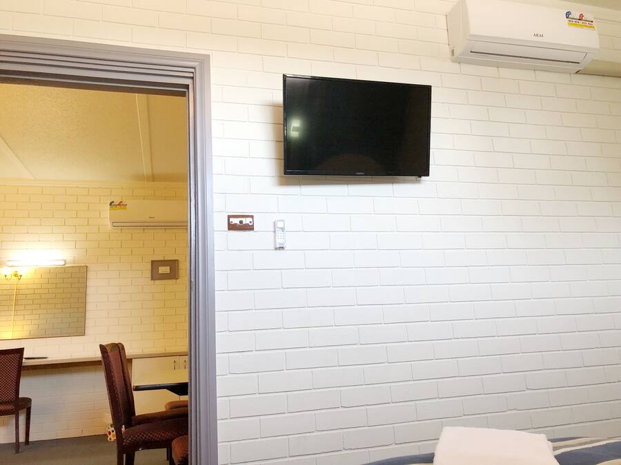 A room with a white brick wall, a flat-screen TV mounted above a whiteboard, and a door leading to another room.