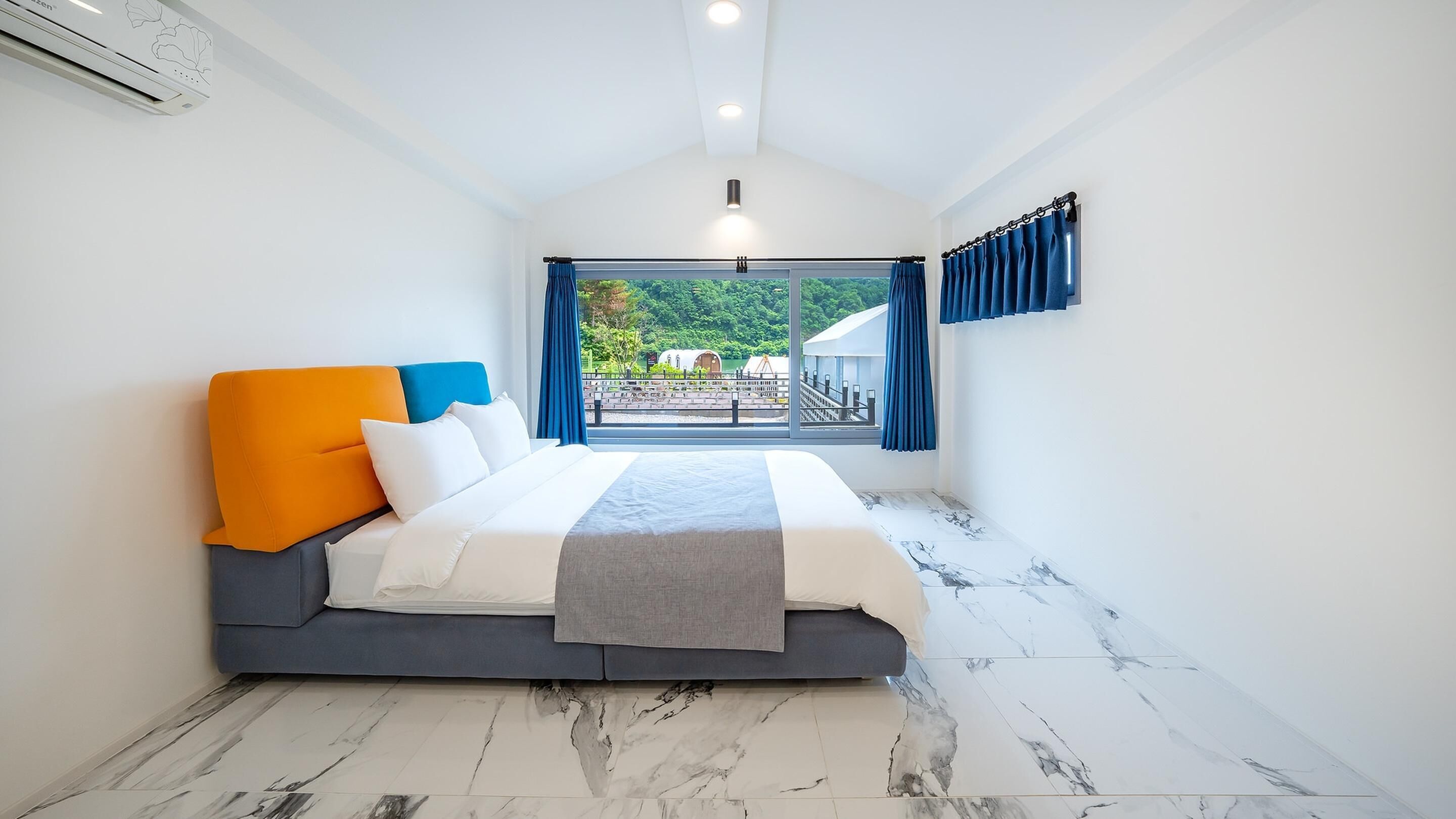 A bedroom with a bed, a window with curtains, and a view of greenery outside.