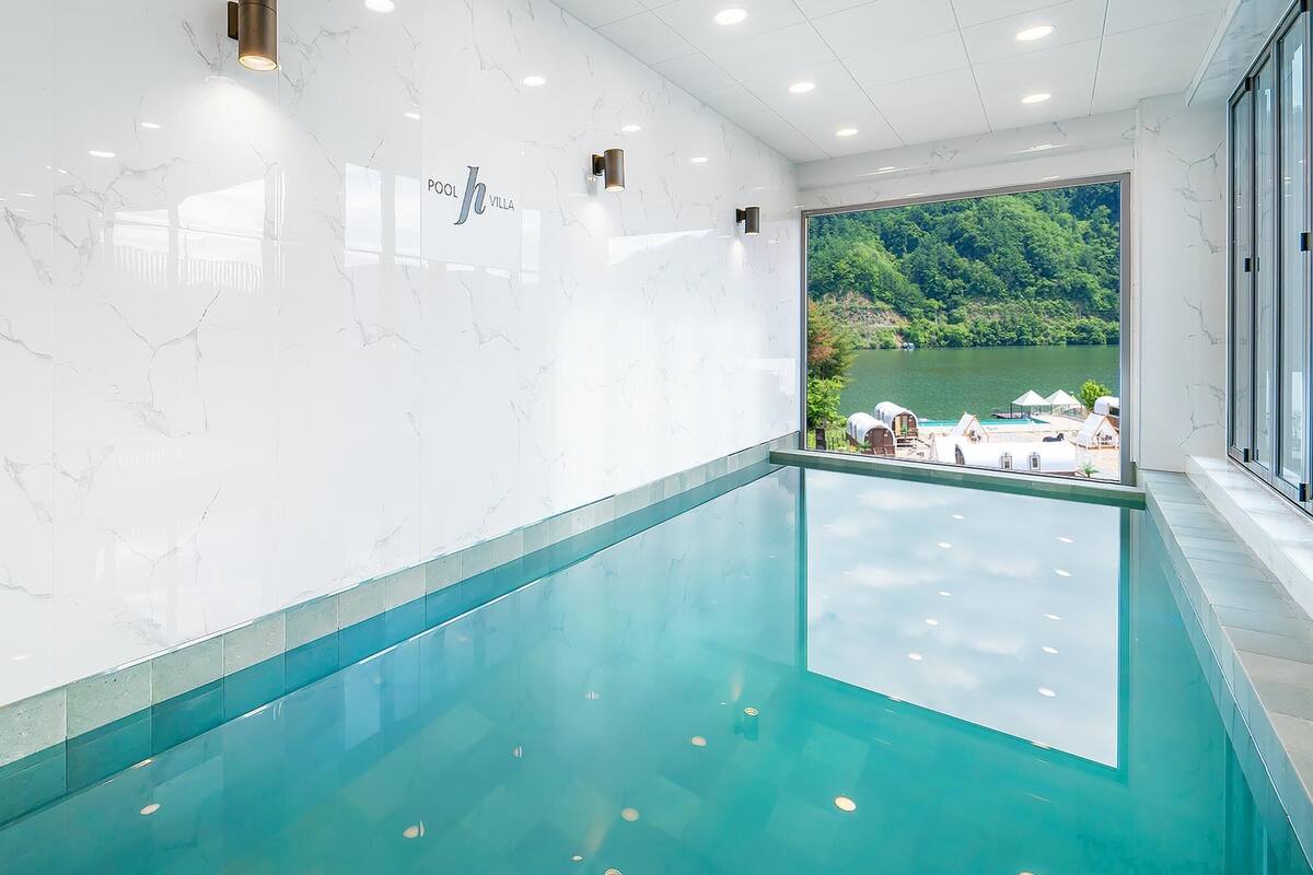 Une piscine intérieure moderne offrant une vue dégagée sur un lac et la verdure environnante.