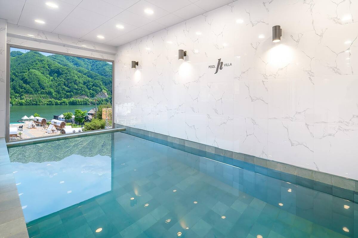 Une piscine intérieure moderne offrant une vue dégagée sur un paysage verdoyant et un lac situé à l’extérieur.