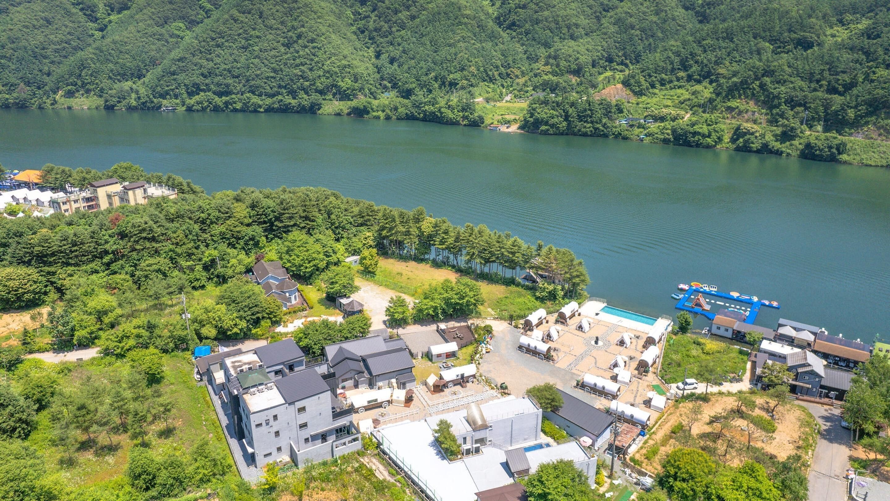 Vue aérienne d’une propriété au bord du lac, comprenant plusieurs bâtiments, dont une grande maison avec une piscine et un quai avec des bateaux.