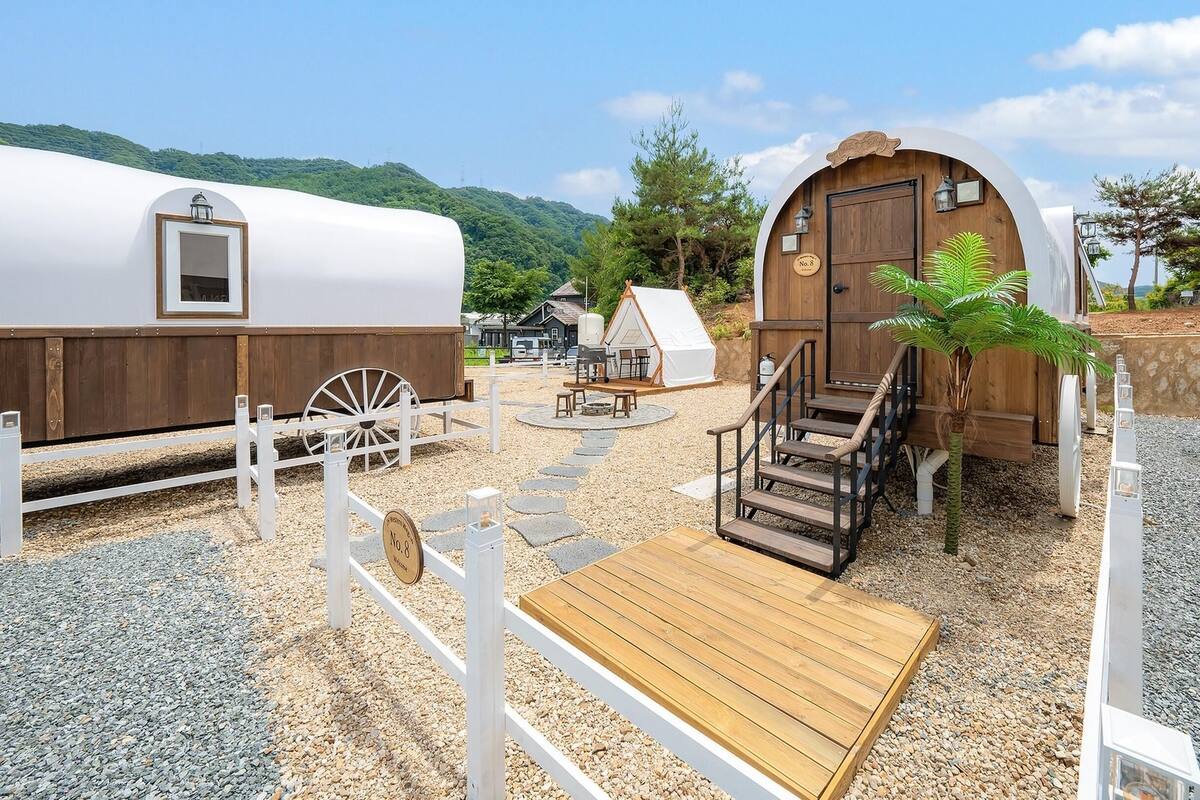 Un terrain de camping rustique avec une tente blanche, une cabane en bois et une terrasse en bois.