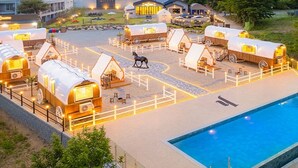 Un complejo turístico con varias cabañas cubiertas, una piscina y un edificio grande al fondo.