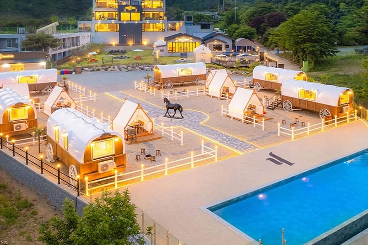 Un complexe hôtelier comprenant plusieurs chalets couverts, une piscine et un grand bâtiment en arrière-plan.