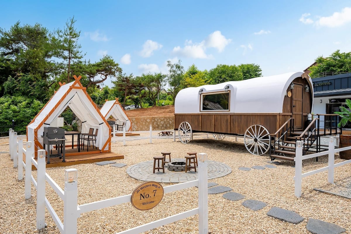 Un chariot couvert doté d’une cabine en bois, d’un espace repas avec des tables et des chaises, et d’une enseigne sur laquelle on peut lire : « Bienvenue ».