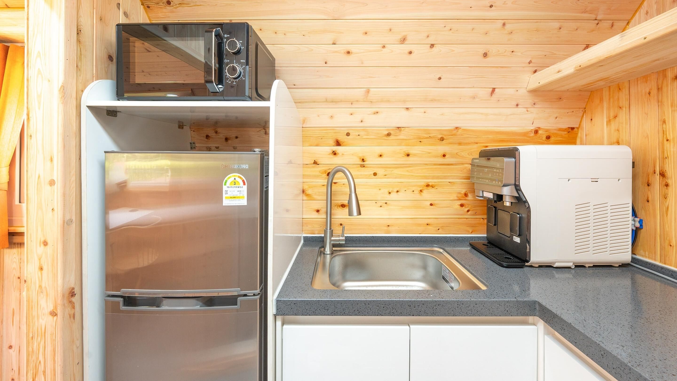 A compact kitchen with a stainless steel refrigerator, a microwave, a coffee machine, and a sink.
