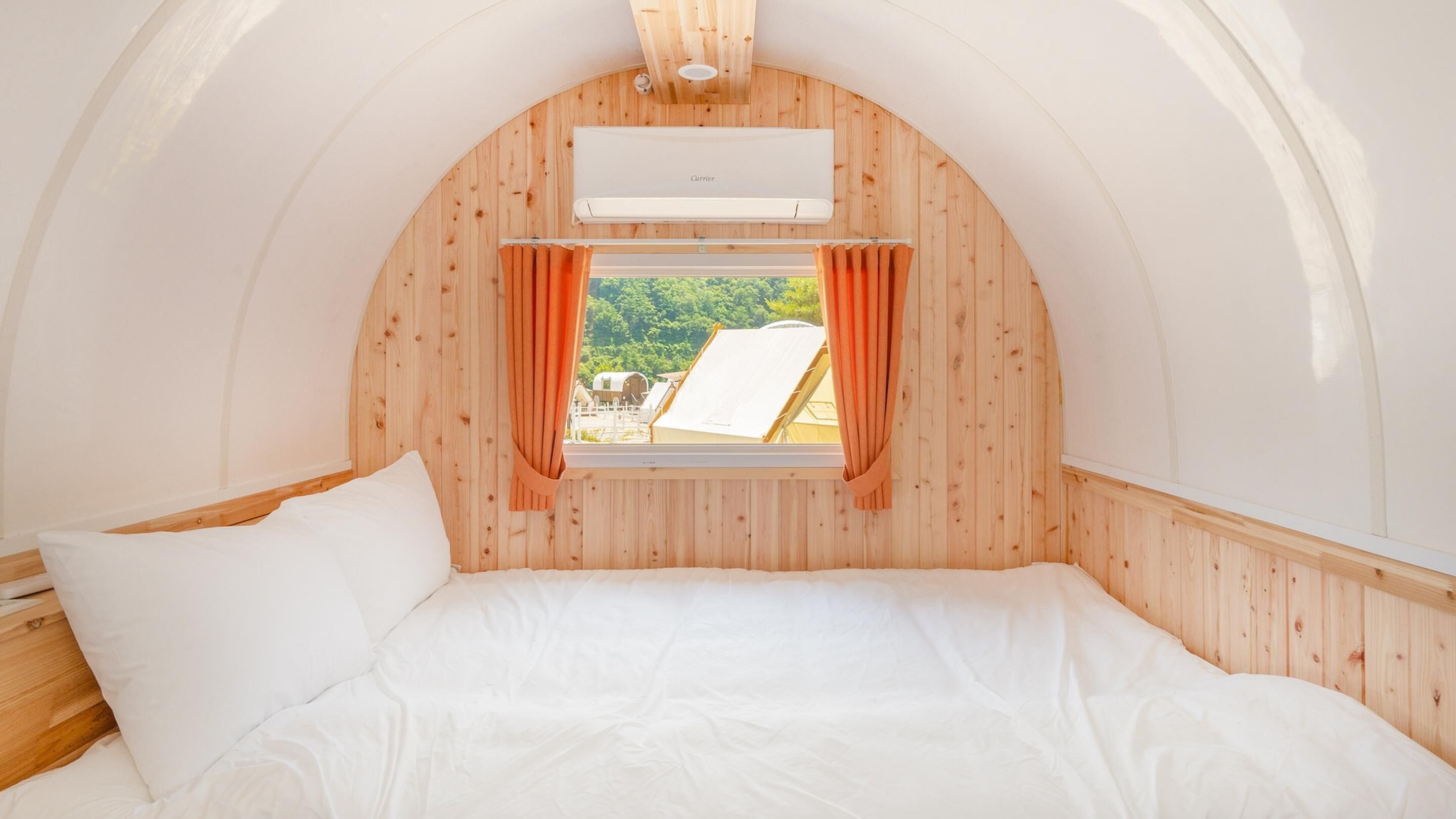 Ein gemütlicher Raum mit Holzwänden, einem Bett, einem Fenster mit Vorhängen und einer Klimaanlage.