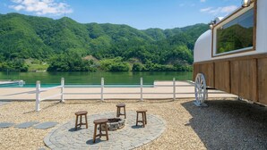 Terraza a la orilla del lago con un brasero, asientos y vistas al lago y colinas boscosas.