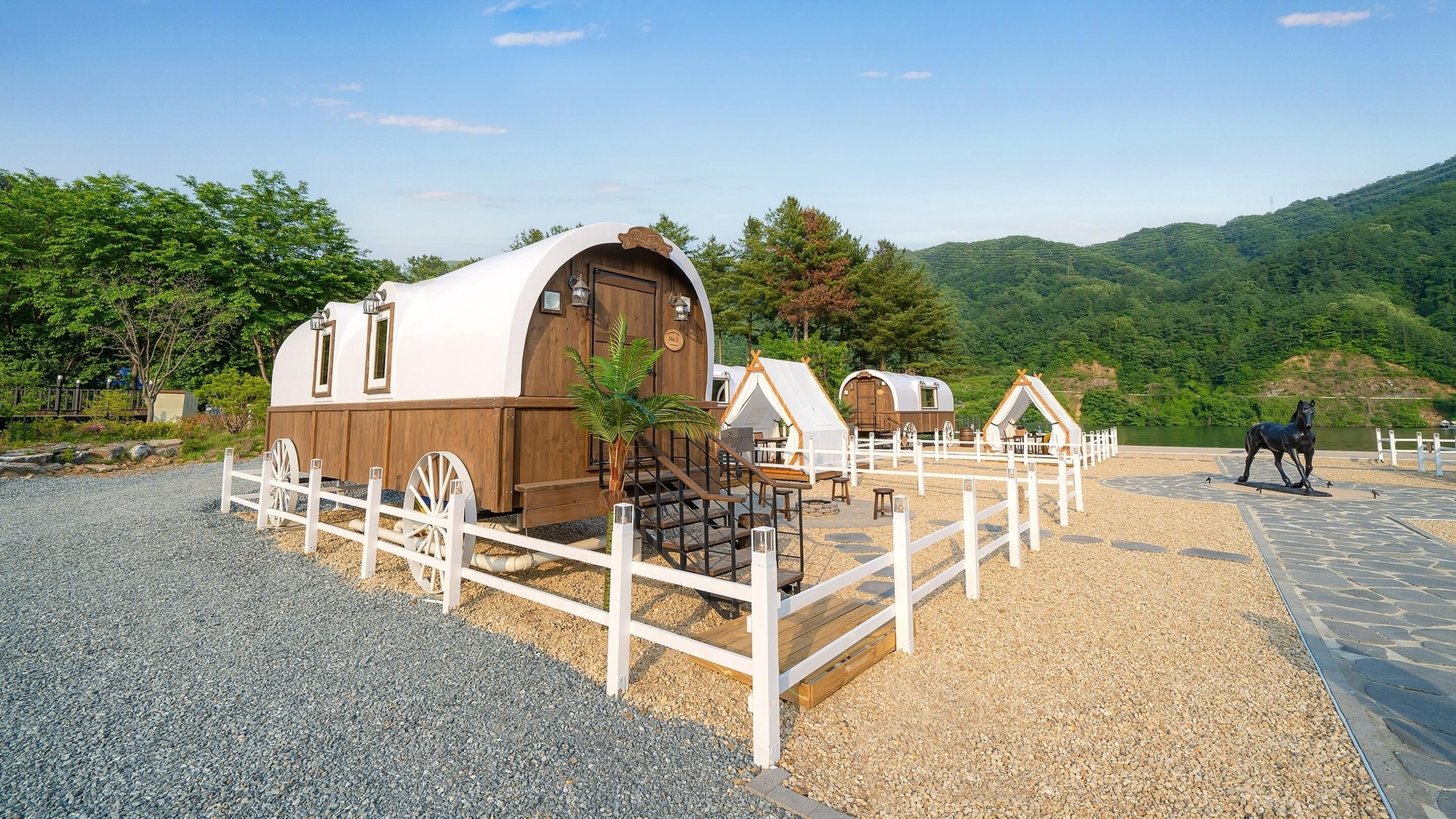 A rustic caravan-style accommodation with a white and brown exterior, a fenced outdoor seating area, and a scenic mountainous backdrop.
