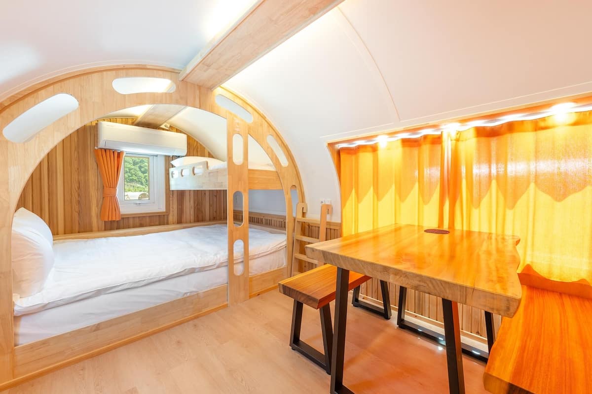 Un intérieur chaleureux avec des lits superposés en bois, une table en bois et un espace éclairé d’une lumière douce.