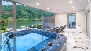 Un moderno espacio de spa con un jacuzzi, ventanas amplias y vistas a un lago y un bosque.
