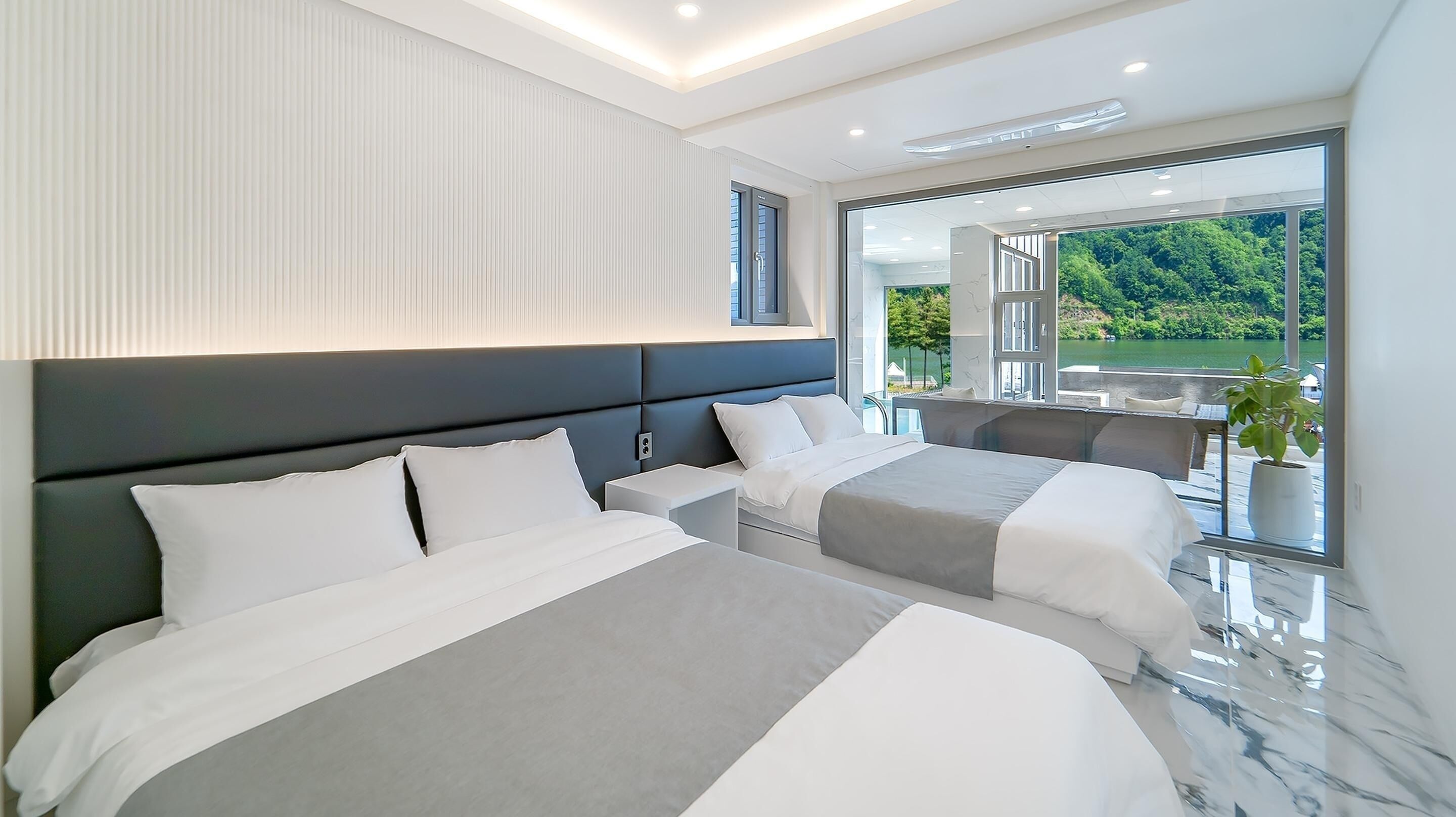 Una habitación de hotel moderna con dos camas, un balcón y vistas al lago, además de un gran ventanal.