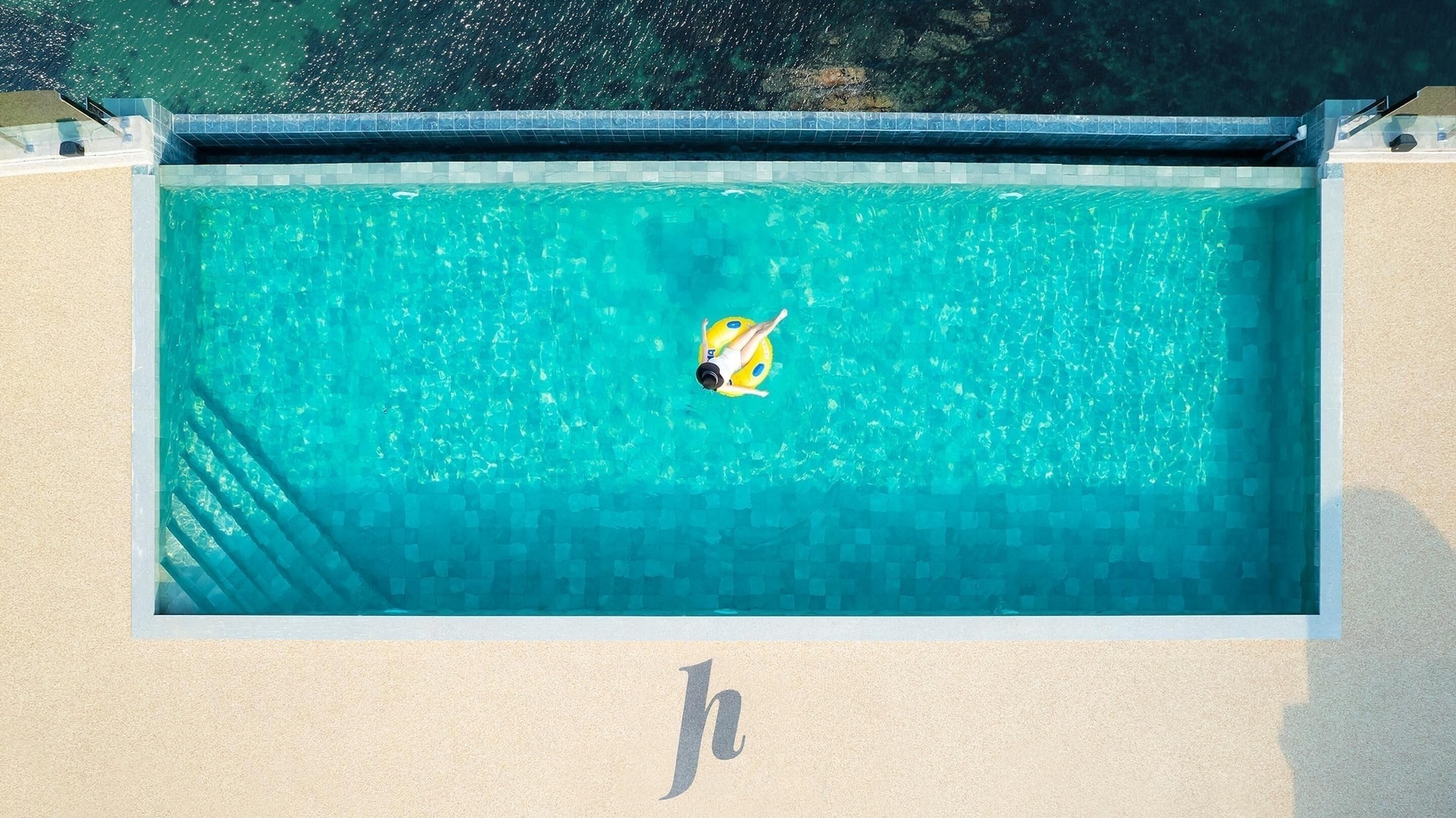 Una piscina rectangular con agua cristalina azul, rodeada por una solana con baldosas y una zona de arena.