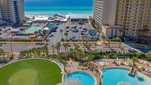 A hotel with multiple swimming pools, a parking lot, and a view of the ocean.