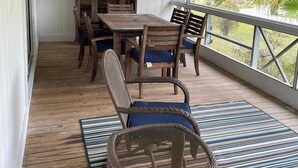 Un patio cubierto con mesa y sillas de madera, ventiladores de techo y vistas a la vegetación.