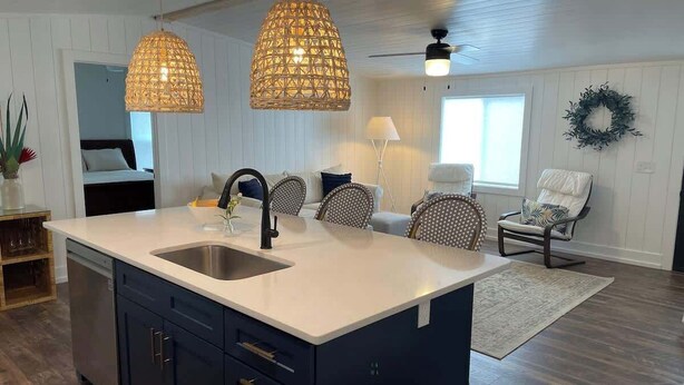 Una cocina moderna con una isla central, dos lámparas colgantes y una zona de comedor con sillas.