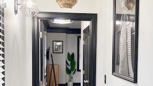 A hallway with a wooden floor, a framed picture of a crown, and a potted plant.