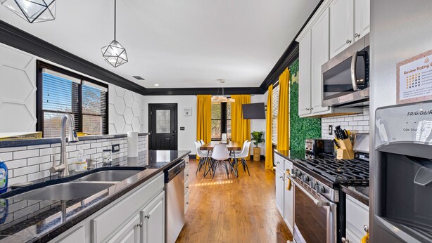 A modern kitchen with white cabinets, a black countertop, a stove, and a refrigerator. There is a dining area with a table and chairs.