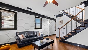 A modern living room with a black leather sofa, a wooden coffee table, and a staircase with wooden railings.