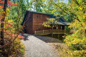 A rustic cabin with a wooden exterior, a covered porch, and a stone pathway leading to it.