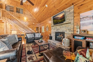 A log cabin interior with a fireplace, leather sofas, a coffee table, and a staircase.