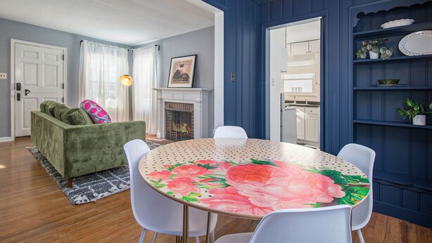 A dining area with a round table, white chairs, a green sofa, and a blue wall. - Shamrock Sanctuary walkable to Notre Dame 1.5 mi (South Bend)