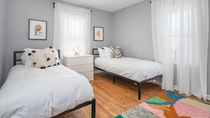 A bedroom with two beds, a nightstand, and a colorful rug. - Shamrock Sanctuary walkable to Notre Dame 1.5 mi (South Bend)