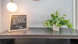 A framed welcome sign with a light bulb on a dark surface, next to a potted plant. - Shamrock Sanctuary walkable to Notre Dame 1.5 mi (South Bend)