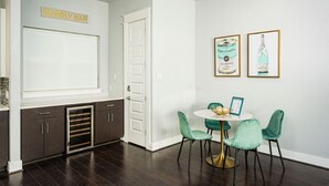 Una cocina con un letrero que dice 'BUBBLY BAR', una puerta blanca y un comedor con una mesa redonda y sillas verdes.