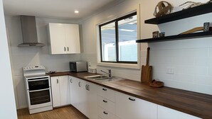 A modern kitchen with white cabinets, a double oven, a microwave, and a wooden countertop. - Minutes to the beach! Freshly renovated, stylish & modern. (Hardwicke Bay)