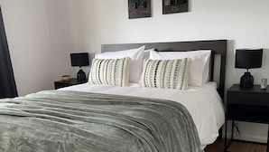 A neatly made bed with a grey blanket, two bedside tables with lamps, and two wall-mounted artworks. - Minutes to the beach! Freshly renovated, stylish & modern. (Hardwicke Bay)
