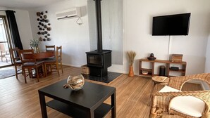 A living room with a fireplace, a TV mounted on the wall, a dining area with wooden furniture, and a wicker chair. - Minutes to the beach! Freshly renovated, stylish & modern. (Hardwicke Bay)