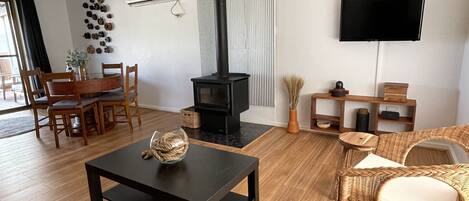 Una sala de estar con chimenea, un televisor montado en la pared, un comedor con muebles de madera y una silla de mimbre.