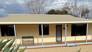 A single-story building with a flat roof, a covered porch, and a gravel driveway. - Minutes to the beach! Freshly renovated, stylish & modern. (Hardwicke Bay)