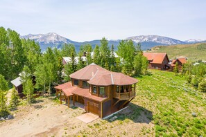 A wooden cabin with a large deck and a mountain backdrop. - Mt CB Home | 3 Bedrooms | Amazing Mountain Views | Hot Tub | Gas Grill (Mt. Crested Butte)