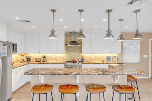 Cozinha moderna com armários brancos, bancada de granito e uma ilha central com banquetas.