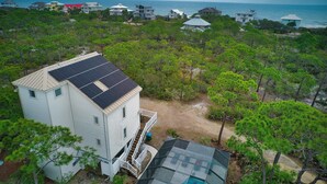 Una propiedad costera con una casa que cuenta con paneles solares, rodeada de abundante vegetación y vistas al océano.