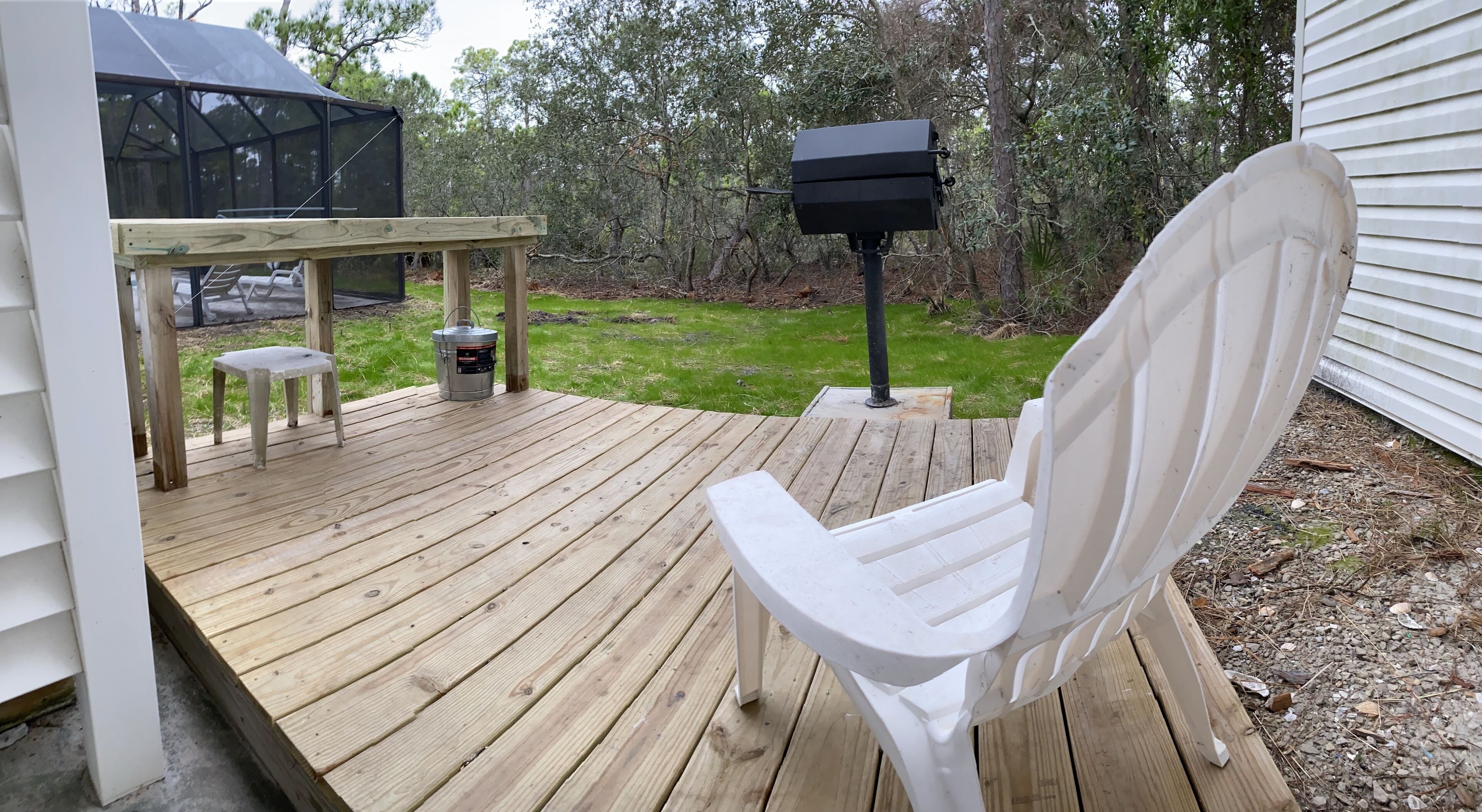 Eine Holzterrasse mit einem weißen Stuhl, einem Grill und einem Mülleimer.