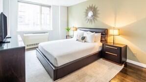 Quarto moderno com cama grande, luminárias de cabeceira, espelho decorativo e janela com persianas.