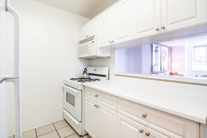 A kitchen with white cabinets, a stove, a microwave, and a refrigerator.