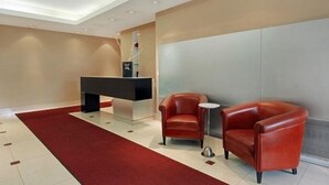 Uma área de recepção com balcão, duas poltronas de couro, uma mesinha lateral e um tapete vermelho.