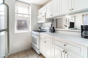 Una cocina con gabinetes blancos, estufa, microondas y cafetera.