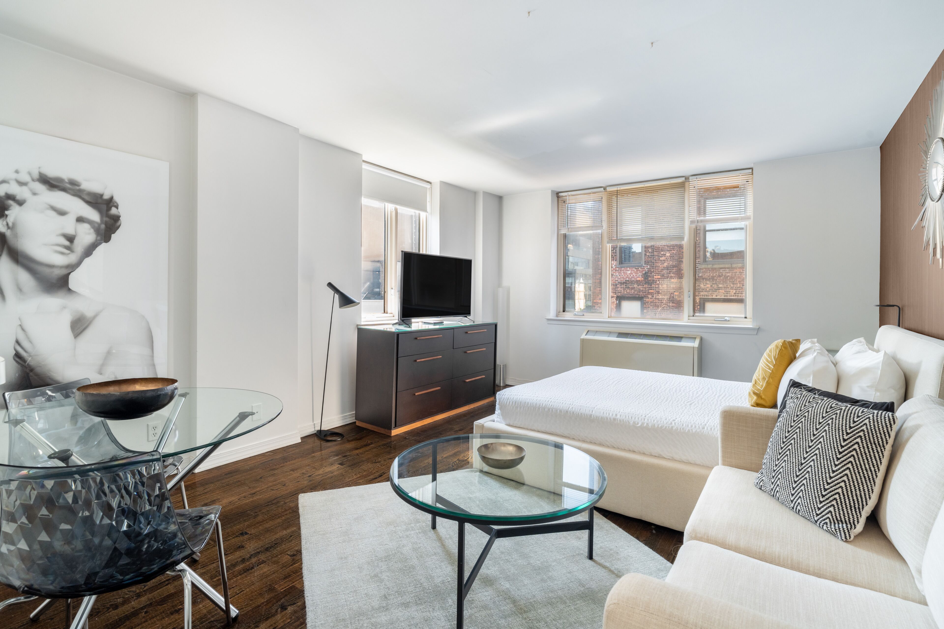 Une chambre moderne avec un lit, une table basse en verre, un canapé, un téléviseur et une grande œuvre d’art accrochée au mur.