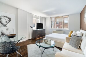Un dormitorio moderno con una cama, una mesa de centro de vidrio, un sofá, un televisor y una obra de arte grande en la pared.