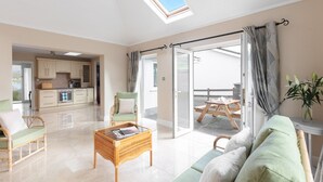 A spacious living room with a sofa, a wicker coffee table, and a view of a patio with a table and chairs. - Bay View Cottage 3 bedroom house VRBO (County Kerry)