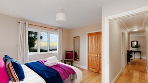 A bedroom with a bed, a window with curtains, a wooden door, and a hallway leading to another room. - Bay View Cottage 3 bedroom house VRBO (County Kerry)