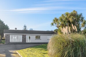 A single-story house with a stone facade, a tiled roof, and a front yard with grass and a palm tree. - Bay View Cottage 3 bedroom house VRBO (County Kerry)